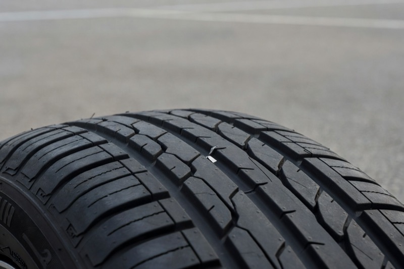 A car tyre on tarmac with a small object embedded in the tread