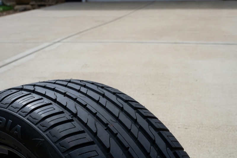 A close view of a car tyre tread on a driveway, showing the grooves and wear