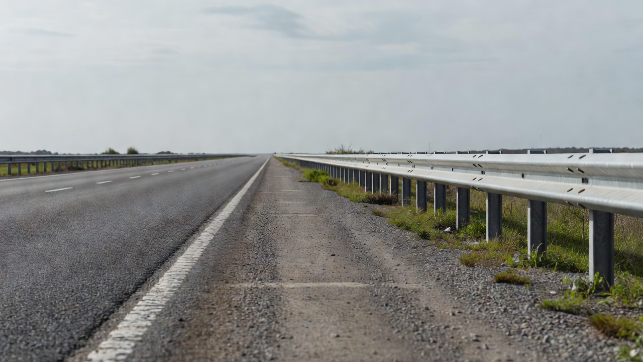 An empty road shoulder beside a crash barrier in flat daylight